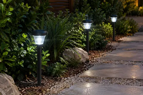 Trois spots solaires à piquer éclairent un chemin de jardin au crépuscule.