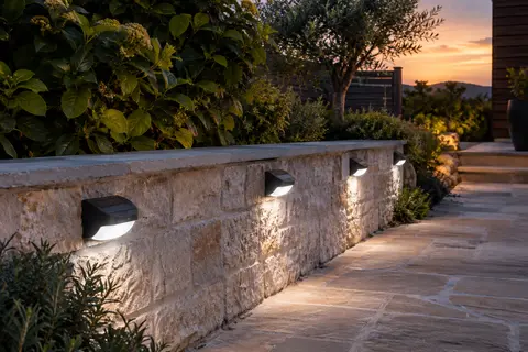 Quatre appliques solaires murales noires éclairent une allée de jardin au crépuscule.