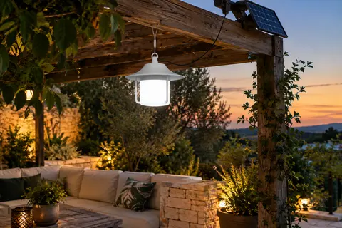 Lampe solaire suspendue blanche sous une pergola, avec panneau orientable séparé et feuillage au crépuscule.