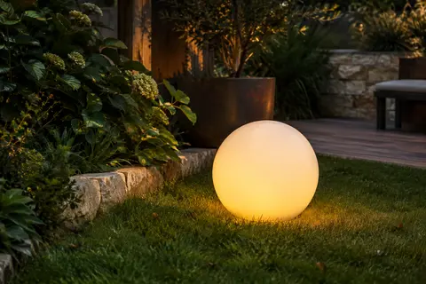 Boule solaire blanche diffusant une lumière colorée dans un jardin au crépuscule