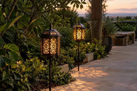 Deux lanternes solaires en métal ajouré sur piquets projettent des motifs lumineux dans un jardin au crépuscule.