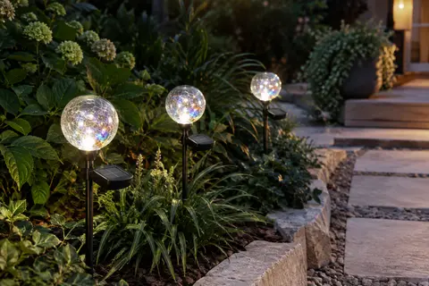 Trois boules solaires en verre craquelé illuminent une allée de jardin au crépuscule.