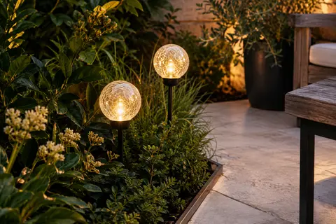 Deux boules solaires en verre craquelé diffusent une lumière blanc chaud près d’une terrasse végétalisée.