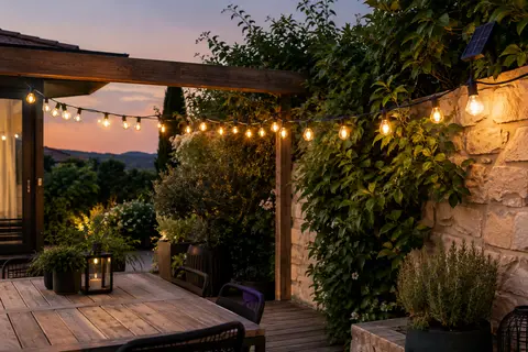 Guirlande solaire à ampoules blanc chaud installée sur une terrasse au milieu de feuillages