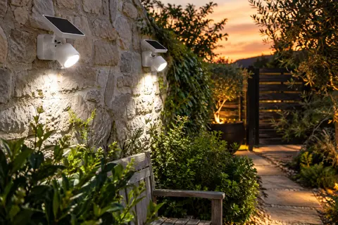 Deux projecteurs solaires blancs fixés sur un mur de jardin, éclairant une allée au crépuscule.