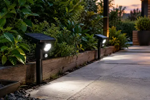 Deux spots solaires noirs avec détecteur éclairent une allée de jardin au crépuscule.