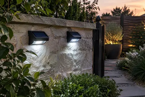 Deux projecteurs solaires compacts éclairent un mur de jardin et un passage au crépuscule.