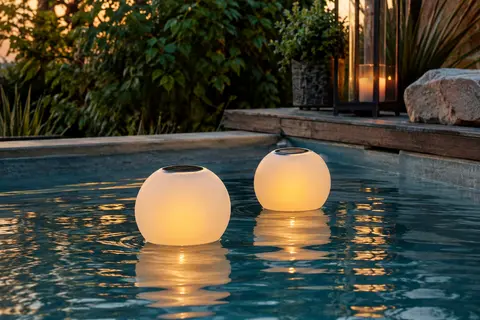 Deux lampes solaires flottantes à effet flamme illuminent doucement la surface d’une piscine au crépuscule.