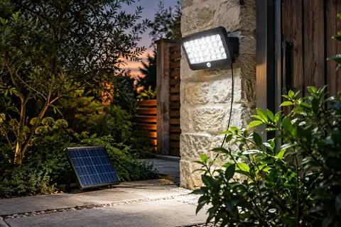 Applique solaire noire à détecteur éclairant un passage de jardin, avec panneau solaire déporté
