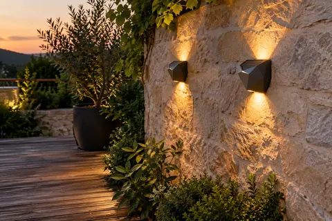 Deux appliques solaires facettées éclairent vers le haut et le bas un mur de pierre au crépuscule.