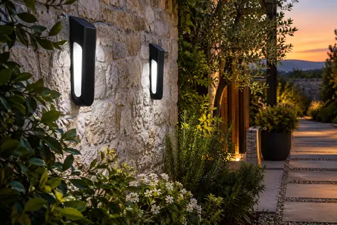 Deux lampes solaires murales noires éclairent une allée de jardin au crépuscule.